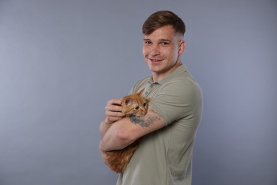 Photo of Man with cute ginger cat on gray background, space for text
