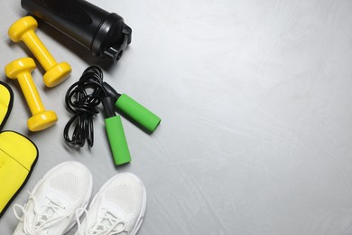 Photo of Sneakers, skipping rope, dumbbells, ankle weights and water bottle on gray textured background, flat lay. Space for text