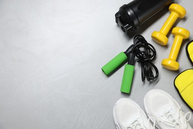 Photo of Sneakers, skipping rope, dumbbells, ankle weights and water bottle on gray textured background, flat lay. Space for text