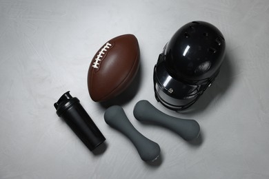 Photo of Protective helmet, American football ball, dumbbells and water bottle on gray textured background, flat lay