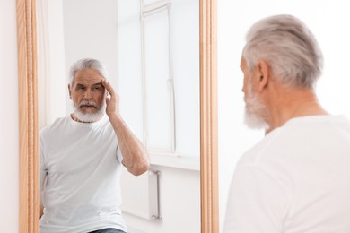 Photo of Handsome senior man looking at himself in mirror indoors
