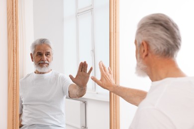 Photo of Handsome senior man looking at himself in mirror indoors