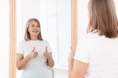 Photo of Beautiful senior woman showing thumbs up near mirror indoors