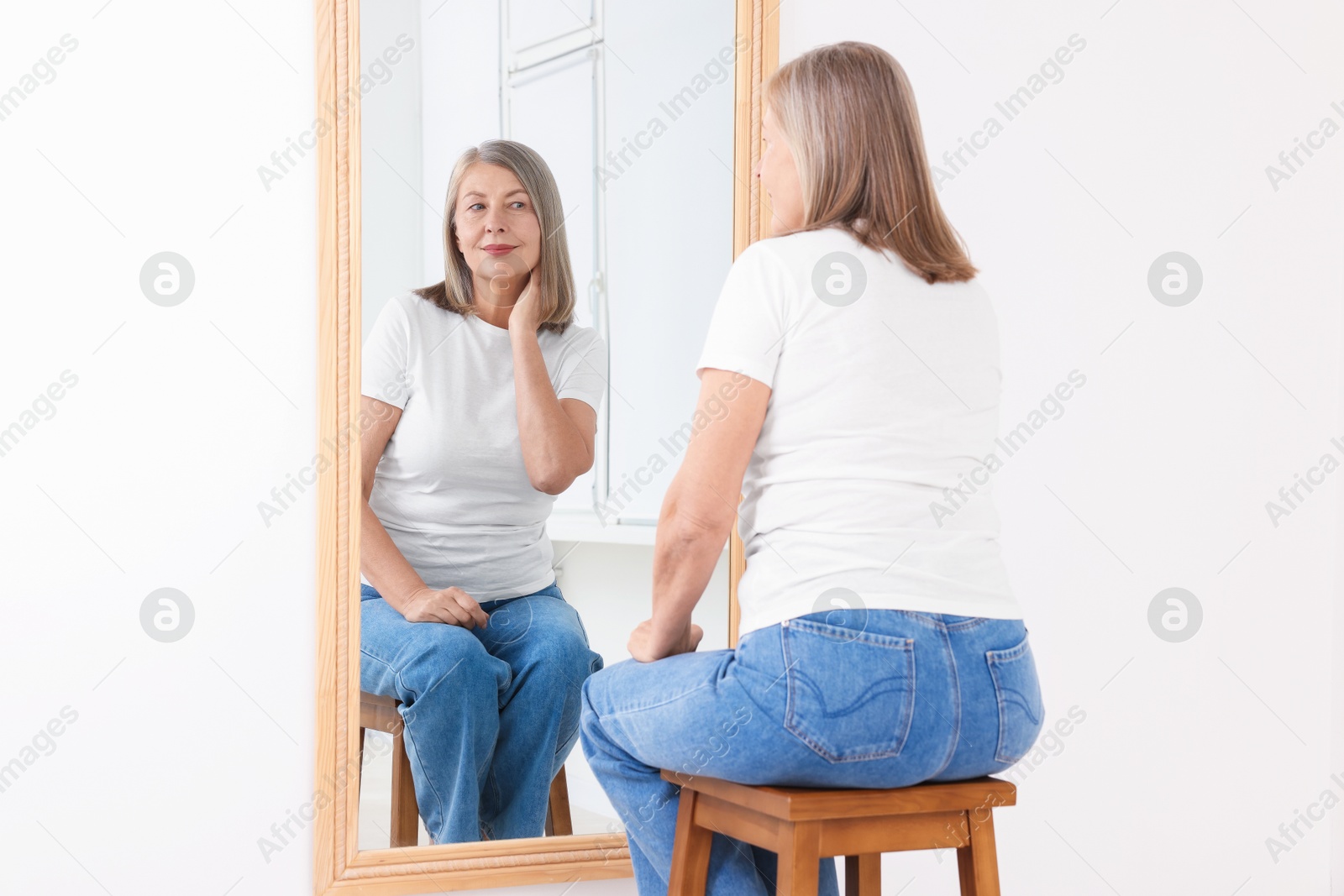 Beautiful senior woman looking at herself in mirror indoors Photo of Beautiful senior woman looking at herself in mirror indoors