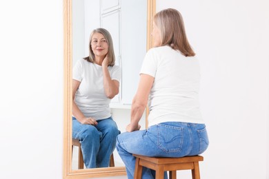 Photo of Beautiful senior woman looking at herself in mirror indoors