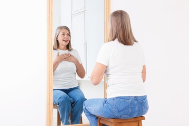 Photo of Beautiful senior woman looking at herself in mirror indoors
