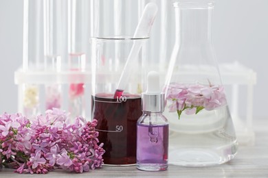Photo of Making luxury perfume. Essential oils in glassware and flowers on white wooden table, closeup