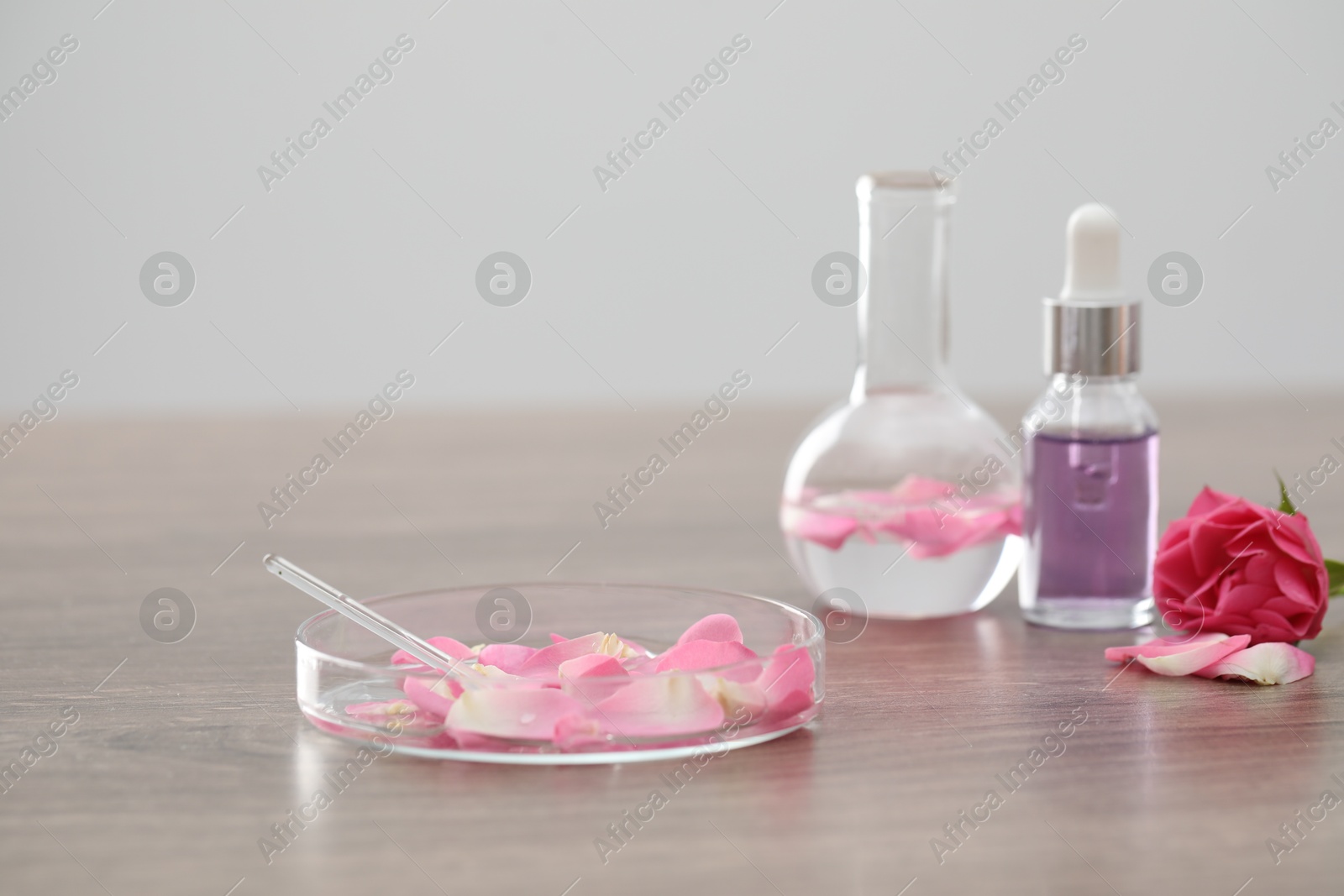 Photo of Making luxury perfume. Essential oils in glassware and flowers on light wooden table, closeup
