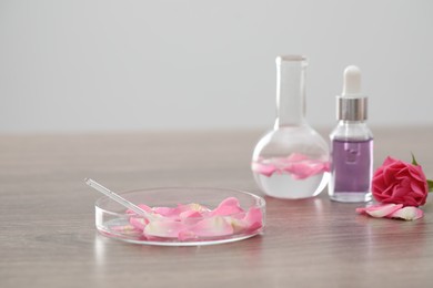 Photo of Making luxury perfume. Essential oils in glassware and flowers on light wooden table, closeup