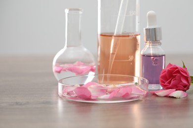 Photo of Making luxury perfume. Essential oils in glassware and flowers on light wooden table, closeup