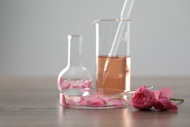 Photo of Making luxury perfume. Essential oils in glassware and flowers on light wooden table, closeup