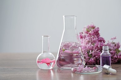Photo of Making luxury perfume. Essential oils in glassware and flowers on light wooden table, closeup. Space for text