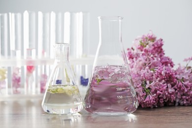 Photo of Making luxury perfume. Essential oils in glassware and flowers on light wooden table, closeup