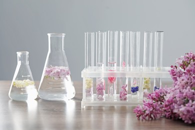 Photo of Making luxury perfume. Essential oils in glassware and flowers on light wooden table, closeup