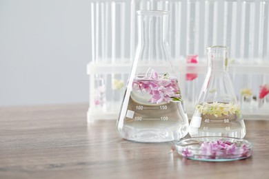Photo of Making luxury perfume. Essential oils in glassware and flowers on light wooden table, closeup. Space for text