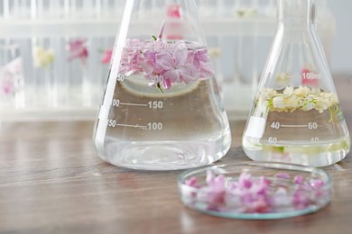 Photo of Making luxury perfume. Essential oils in glassware and flowers on light wooden table, closeup