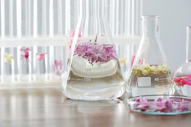 Photo of Making luxury perfume. Essential oils in glassware and flowers on light wooden table, closeup