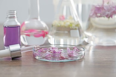 Photo of Making luxury perfume. Essential oils in glassware and flowers on light wooden table, closeup