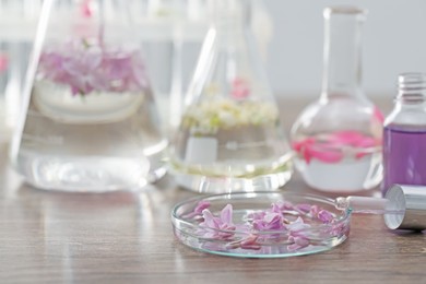 Photo of Making luxury perfume. Essential oils in glassware and flowers on light wooden table, closeup