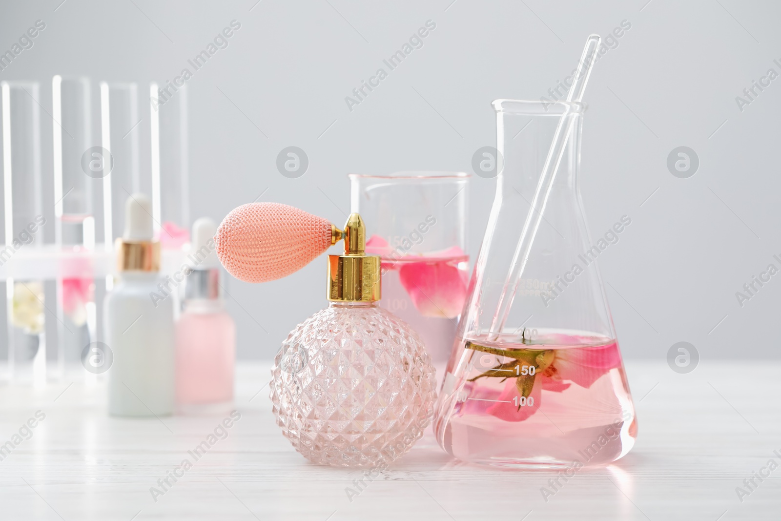 Photo of Making luxury perfume. Essential oils in glassware and flowers on white wooden table, closeup