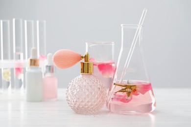 Photo of Making luxury perfume. Essential oils in glassware and flowers on white wooden table, closeup