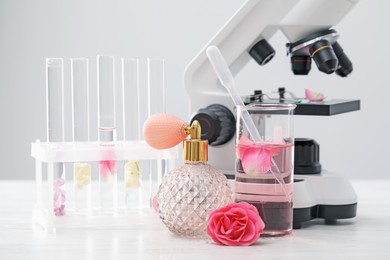 Photo of Making luxury perfume. Essential oils in glassware, flowers and microscope on white wooden table, closeup