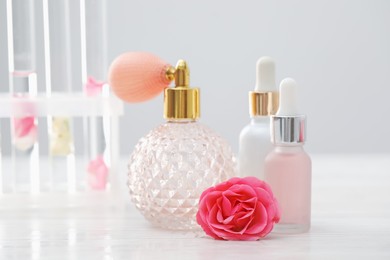 Photo of Making luxury perfume. Essential oils in glassware and flowers on white wooden table, closeup
