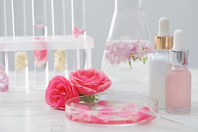 Photo of Making luxury perfume. Essential oils in glassware and flowers on white wooden table, closeup