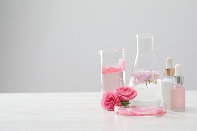 Photo of Making luxury perfume. Essential oils in glassware and flowers on white wooden table, closeup. Space for text