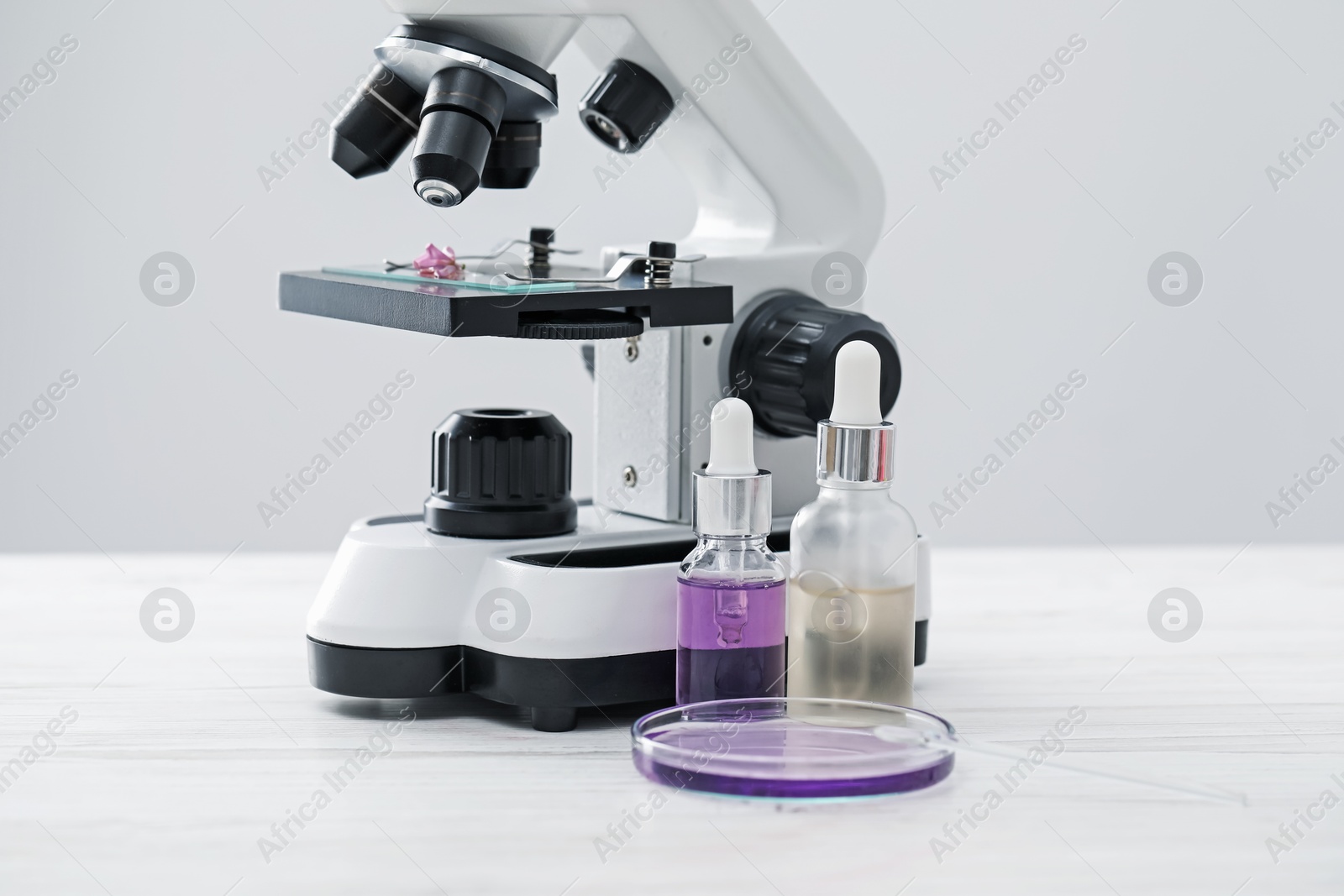 Photo of Making luxury perfume. Essential oils in glassware and microscope on white wooden table, closeup