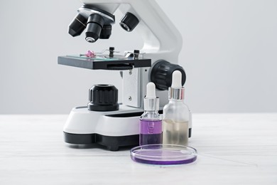 Photo of Making luxury perfume. Essential oils in glassware and microscope on white wooden table, closeup