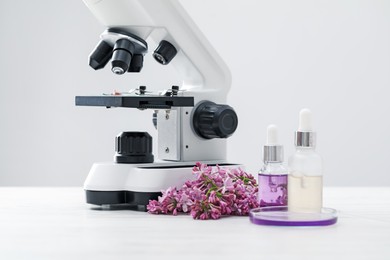 Photo of Making luxury perfume. Essential oils in glassware, flowers and microscope on white wooden table, closeup