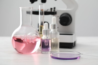 Photo of Making luxury perfume. Essential oils in glassware, flowers and microscope on white wooden table, closeup