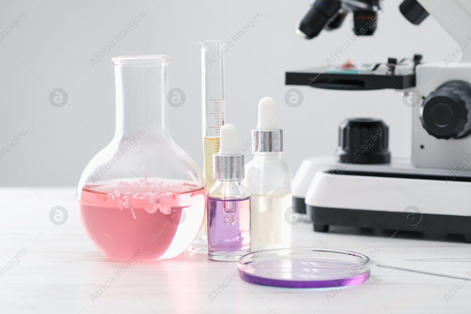 Photo of Making luxury perfume. Essential oils in glassware, flowers and microscope on white wooden table, closeup
