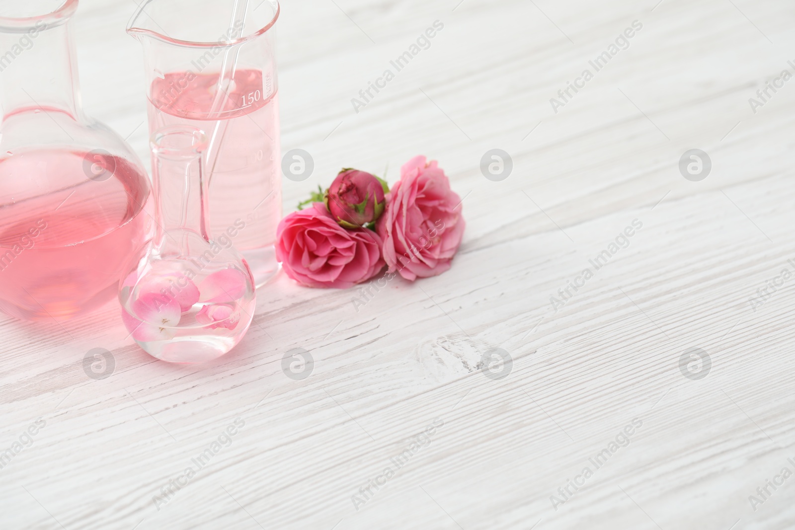 Making luxury perfume. Essential oils in glassware and flowers on white wooden table, closeup. Space for text Photo of Making luxury perfume. Essential oils in glassware and flowers on white wooden table, closeup. Space for text