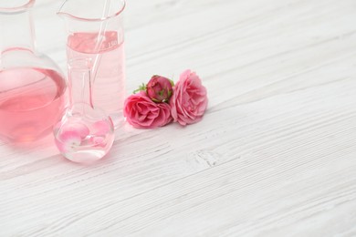 Photo of Making luxury perfume. Essential oils in glassware and flowers on white wooden table, closeup. Space for text