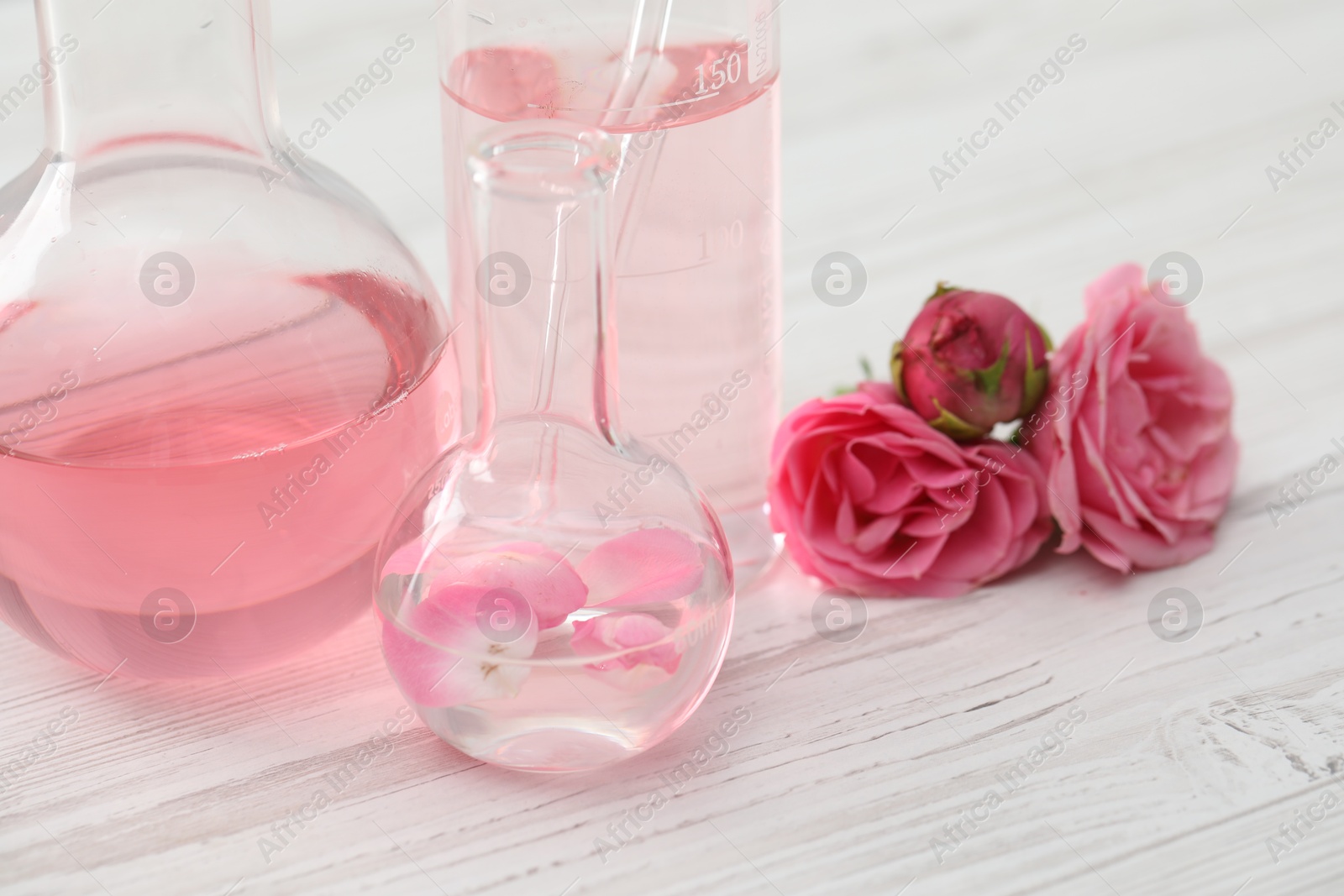 Photo of Making luxury perfume. Essential oils in glassware and flowers on white wooden table, closeup