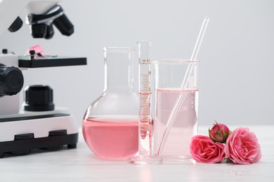 Photo of Making luxury perfume. Essential oils in glassware, flowers and microscope on white wooden table, closeup