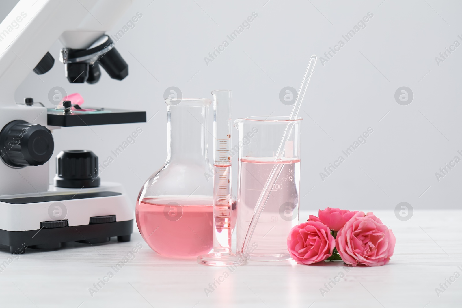 Photo of Making luxury perfume. Essential oils in glassware, flowers and microscope on white wooden table, closeup