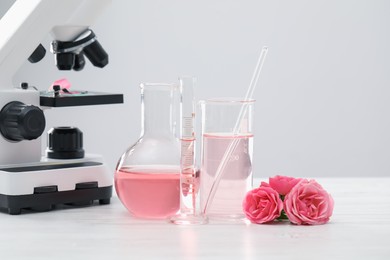 Photo of Making luxury perfume. Essential oils in glassware, flowers and microscope on white wooden table, closeup