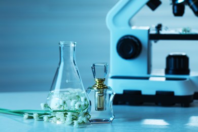 Photo of Making luxury perfume. Essential oils in glassware, flowers and microscope on white wooden table, closeup