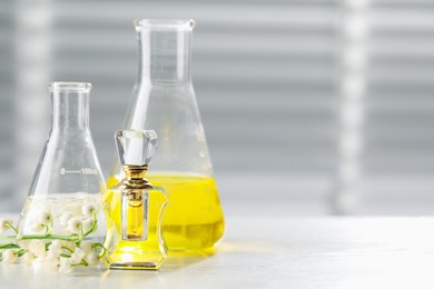 Photo of Making luxury perfume. Essential oils in glassware and flowers on white wooden table, closeup. Space for text