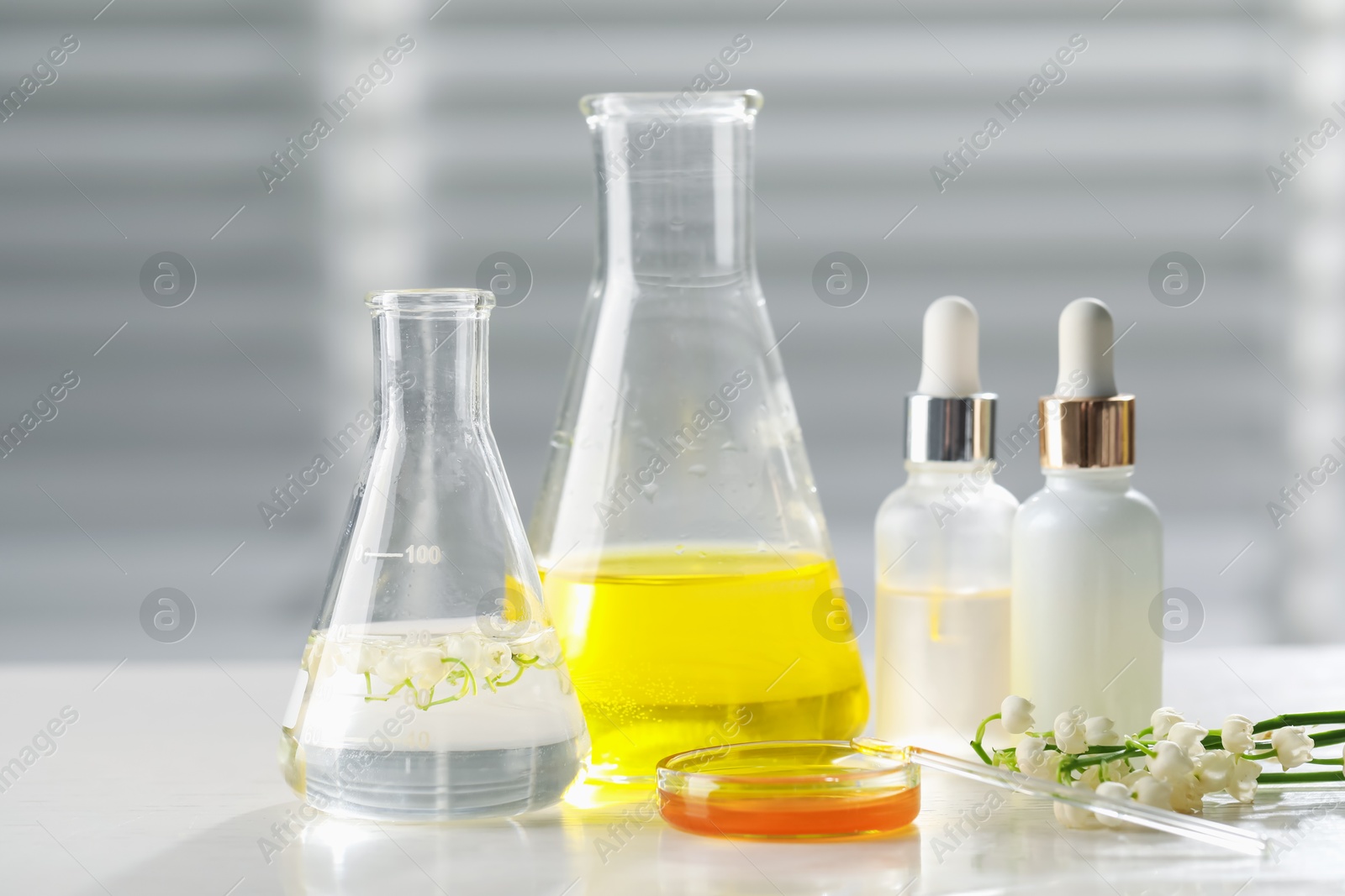 Photo of Making luxury perfume. Essential oils in glassware and flowers on white wooden table, closeup