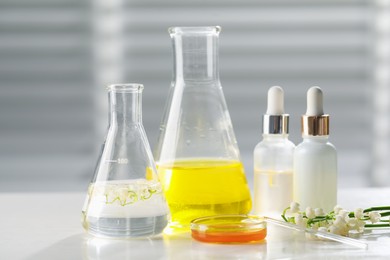 Photo of Making luxury perfume. Essential oils in glassware and flowers on white wooden table, closeup