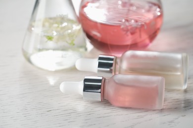 Photo of Making luxury perfume. Essential oils in glassware and flowers on white wooden table, closeup