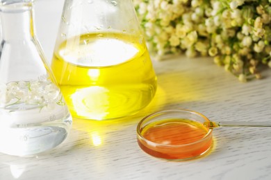 Photo of Making luxury perfume. Essential oils in glassware and flowers on white wooden table, closeup