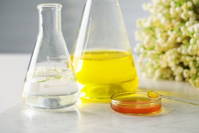 Photo of Making luxury perfume. Essential oils in glassware and flowers on white wooden table, closeup