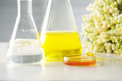 Photo of Making luxury perfume. Essential oils in glassware and flowers on white wooden table, closeup