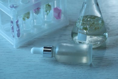 Photo of Making luxury perfume. Essential oils in glassware and flowers on white wooden table, closeup
