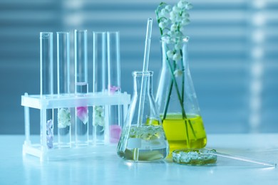 Photo of Making luxury perfume. Essential oils in glassware and flowers on white wooden table, closeup